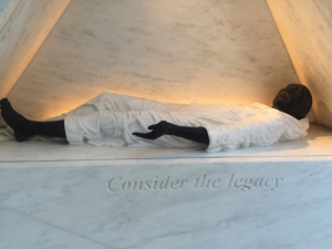 The second element, “Consider the Legacy”, is a full scale human figure lying in front of a wall inscribed with images of the interior of a slave ship. This element abstractly symbolizes the extreme conditions under which millions of African people were transported in the bowels of ships designed for human packing during the Middle Passage. The body appears dignified as though laying in state, or as though they are performing a Graham pleading, which is a physical gesture that requires deep abdominal engagement, embodying a myriad of emotion depending on how it is performed. The depiction of this singular body conveys dignity and not abjection, which is the essence of these centuries of forced migration. It is possible that the artist/architect sought to bring soul to this moment in the similar way that Giambologna depicts the Rape of Sabine which occurred at the founding of Rome circa 750 BC. My experience of the black stone body shrouded in white under a sepia light was marked by contradistinction; I was remembering the historic period but I was also forgetting the visceral heinous nature of the violence inflicted upon my forebears. 